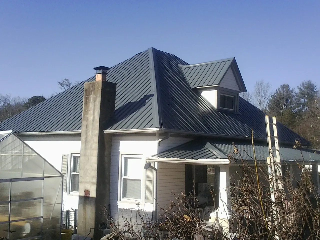 Dark blue standing seam metal roof on a white farmhouse with dormer — Slate & Tile Roof Repair by Roofing Brothers in Iowa City