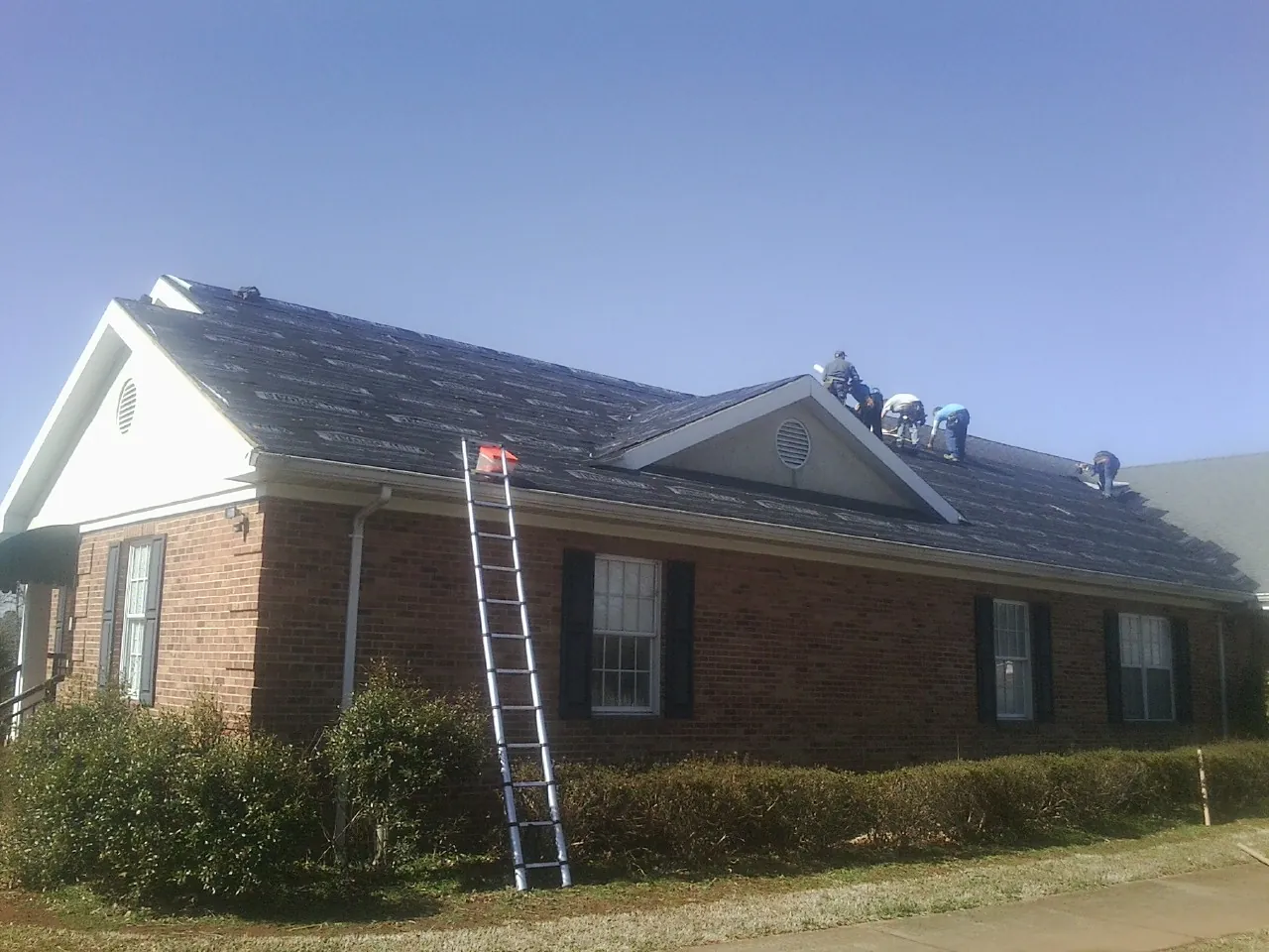 Crew tearing shingles off a brick ranch roof with a ladder set — Metal Roof Repair work by our crew in Iowa City