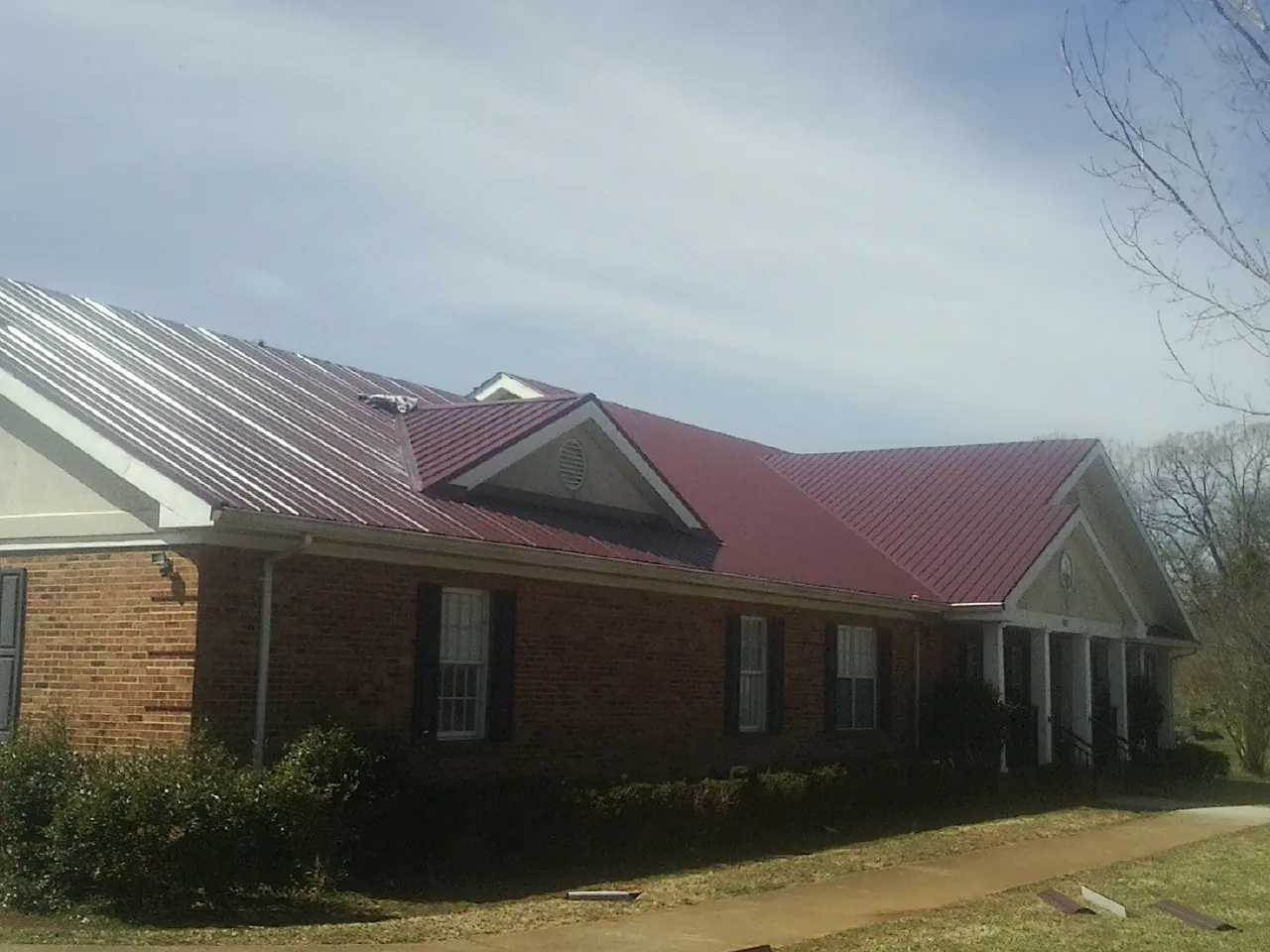 Red metal roof with gabled entries on a long brick building, from a Hail Damage Roof Repair job in Iowa City