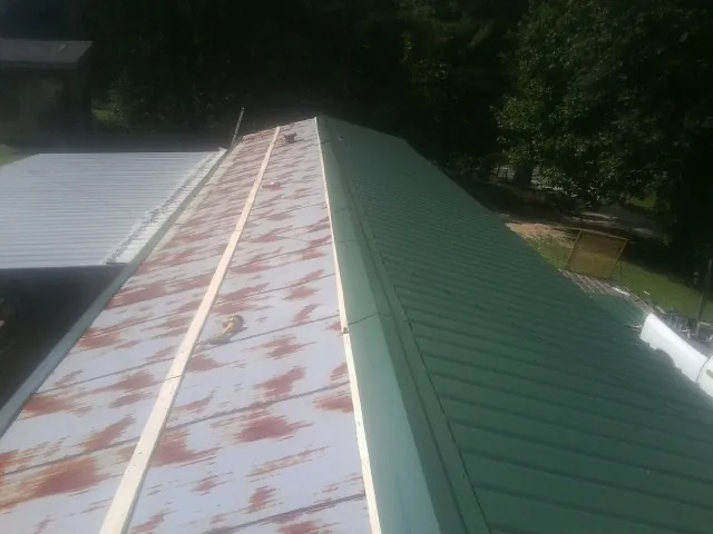 Old rusted panels beside newly installed green metal roofing — Wind Damage Roof Repair by Roofing Brothers in Iowa City