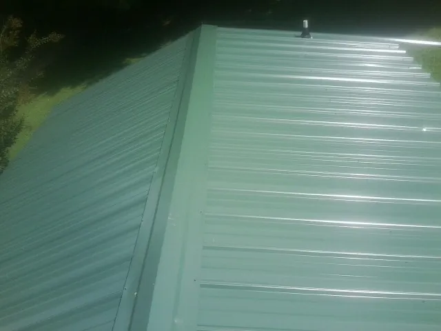 New green metal panels meeting at the ridge of a roof — Flat Roof Repair work by our crew in Iowa City