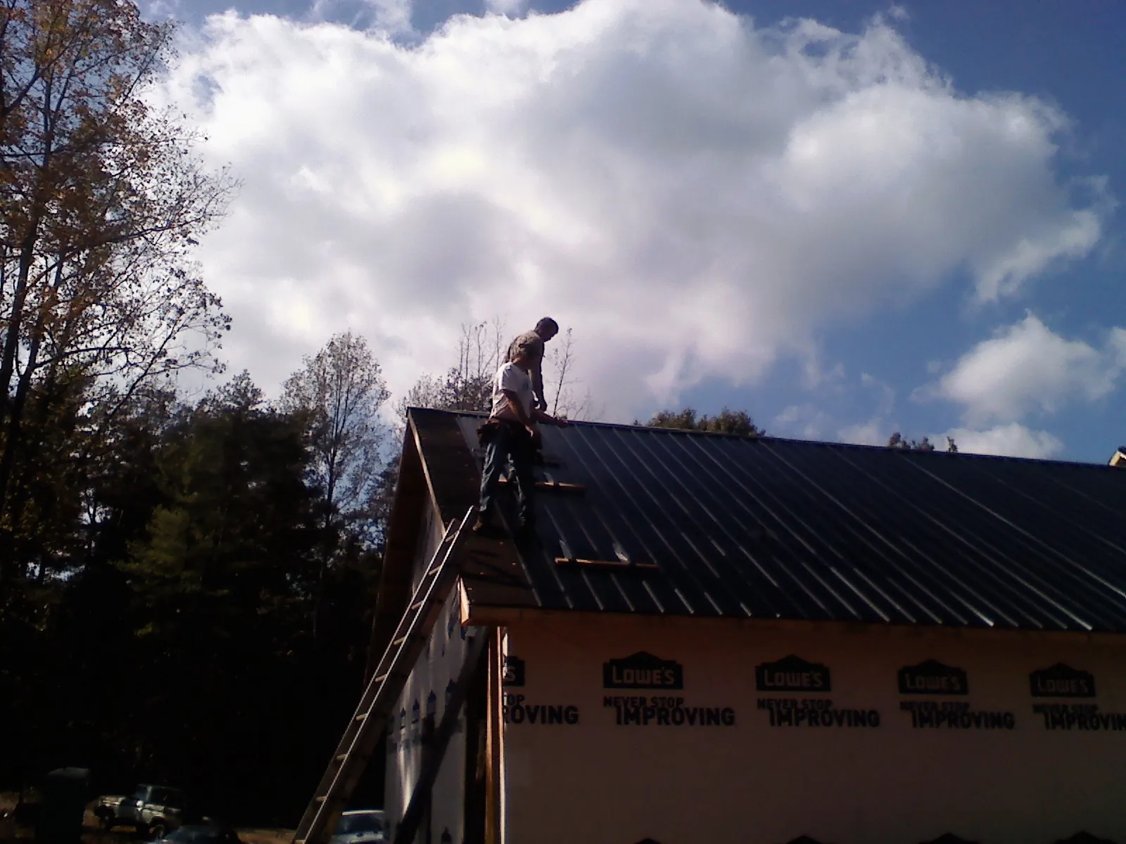 Roofer fastening dark metal panels high against a cloudy sky, from a Roof Inspection job in Iowa City