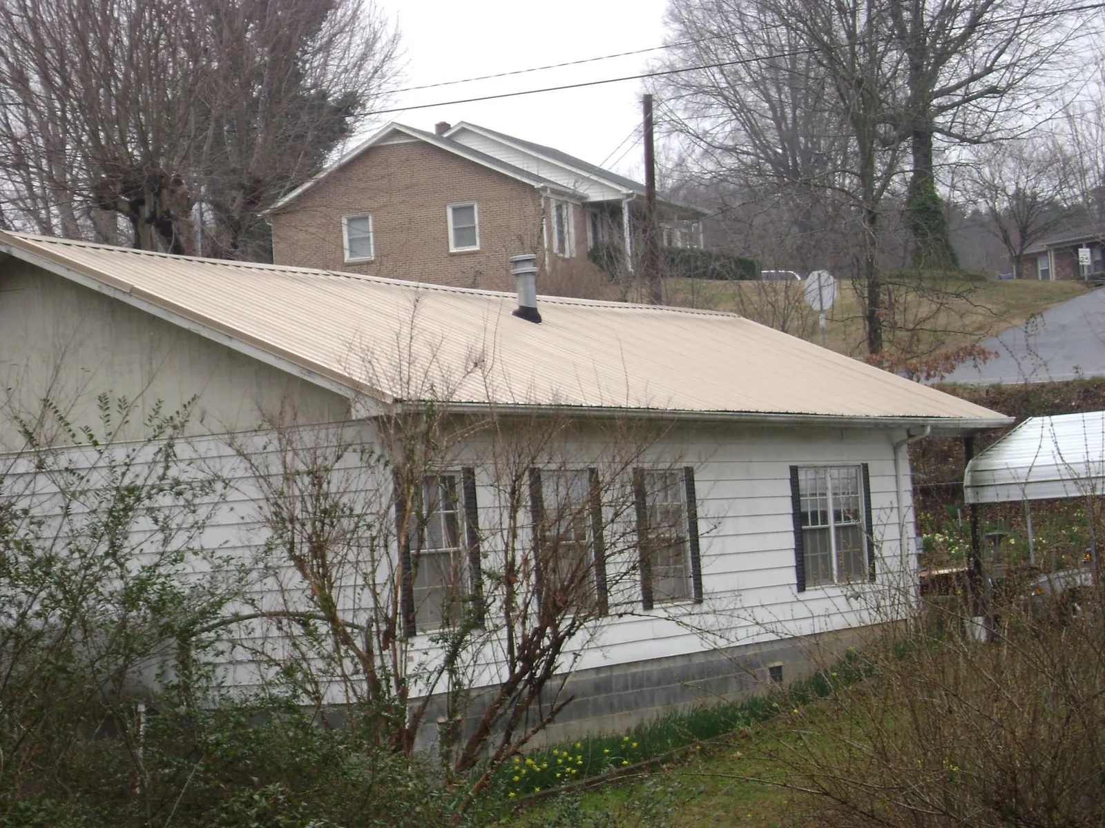 Tan metal roof on a white sided house set into a hillside — Commercial Roofing by Roofing Brothers in Iowa City