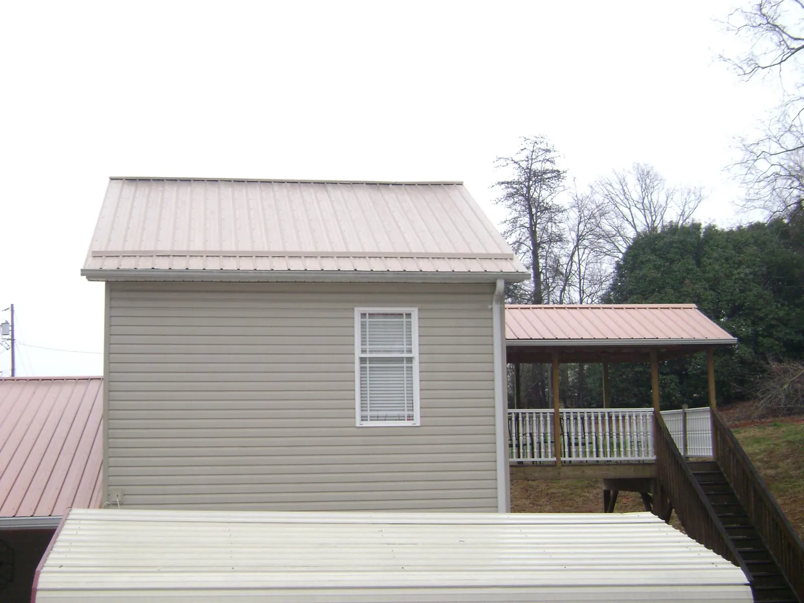 Tan metal roofs on a two story addition and attached porch, from a Roof Replacement job in Iowa City