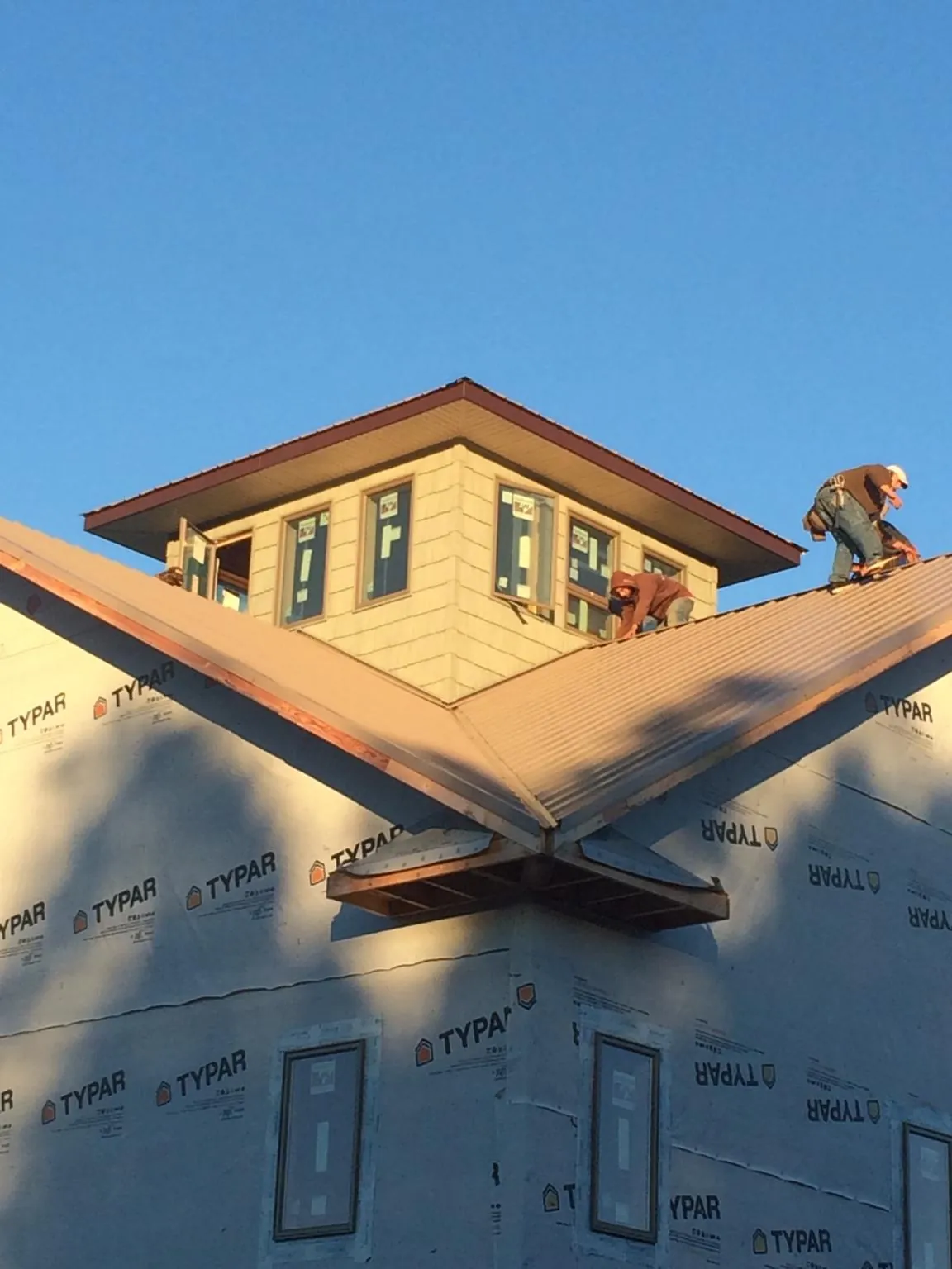 Roofers working around a rooftop cupola on a new metal roof at sunset — Roof Waterproofing in Iowa City by Roofing Brothers